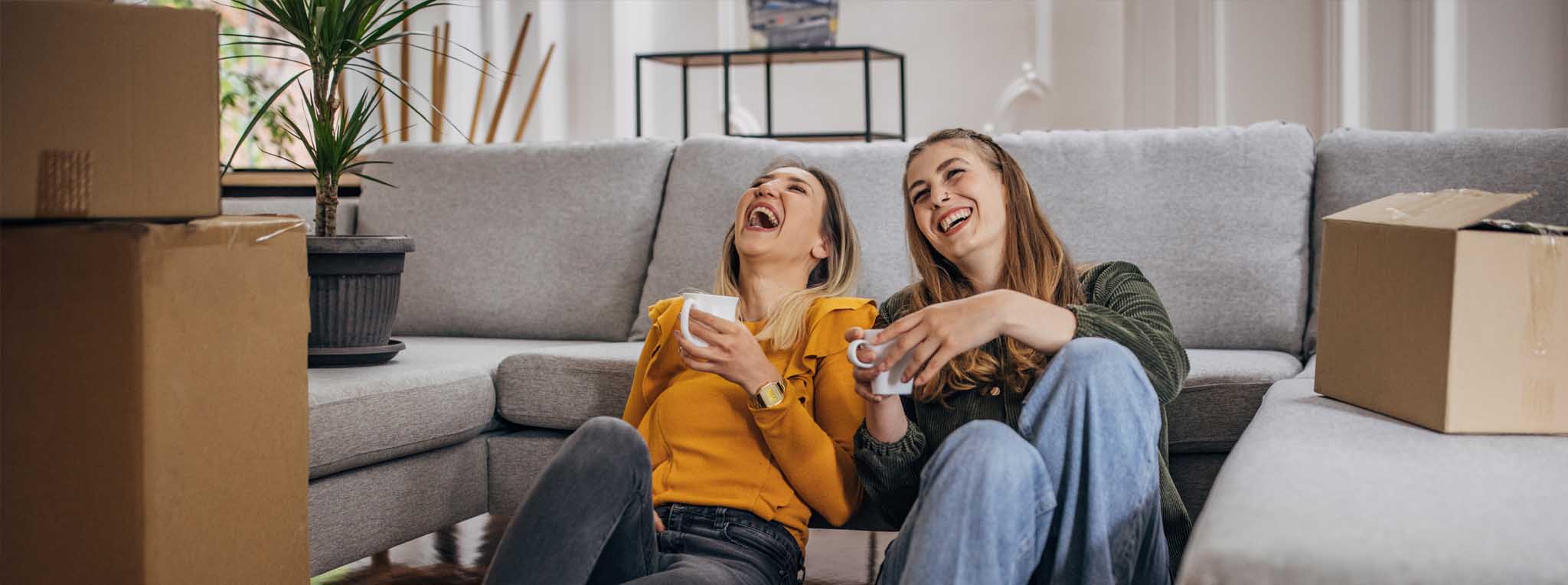 two woman laughing near sofa with boxes